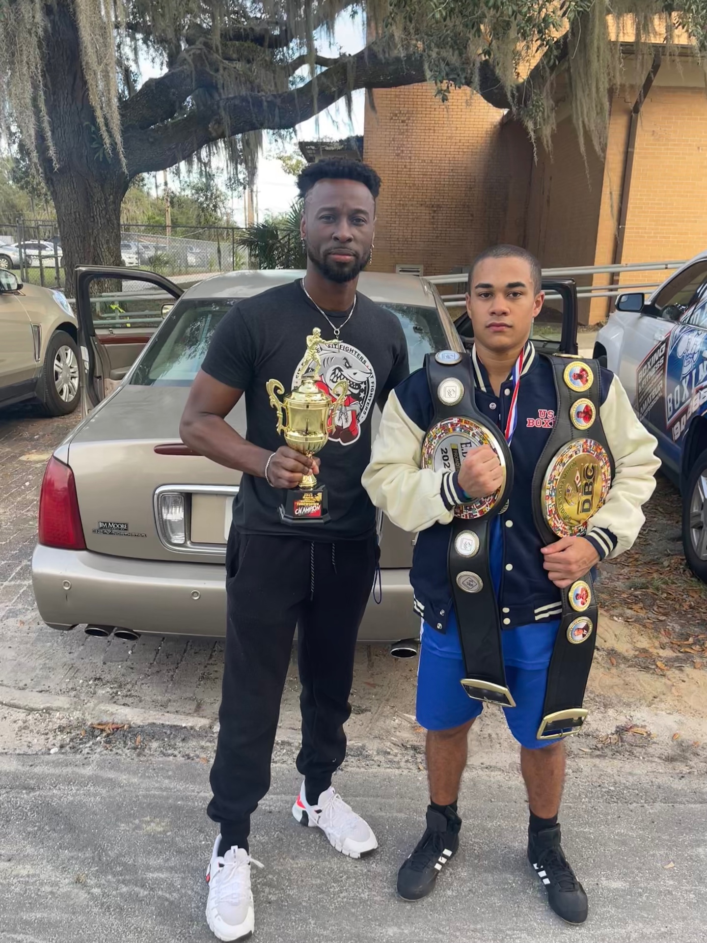 Coach Dom with amateur boxer holding belts and trophy